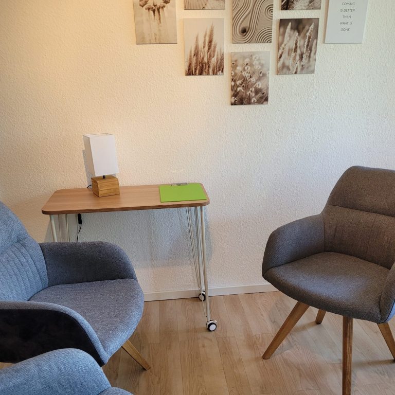 Wand mit Fotos, kleiner Tisch und drei Sessel